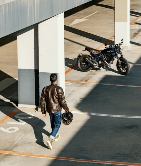 Mann in Lederjacke geht auf Ducati Scrambler zu